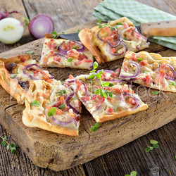 Elsässer Flammkuchen mit Zwiebeln und Speck rustikal auf altem Schneidbrett serviert - Traditional Alsatian tarte flambée  with onions, bacon and sour cream served on a shabby cutting board