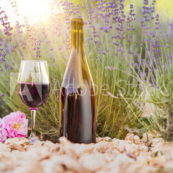 Red wine bottle and wine glass on the ground. Sunset over a summer lavender field in Provence, France.