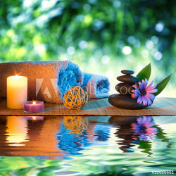 two candles and towels black stones and purple daisy on water
