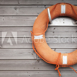 Red lifebuoy with rope on weathered wooden wall
