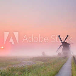 windmill and rising sun in fog