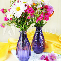 Wildflowers in glass vases on table on light background